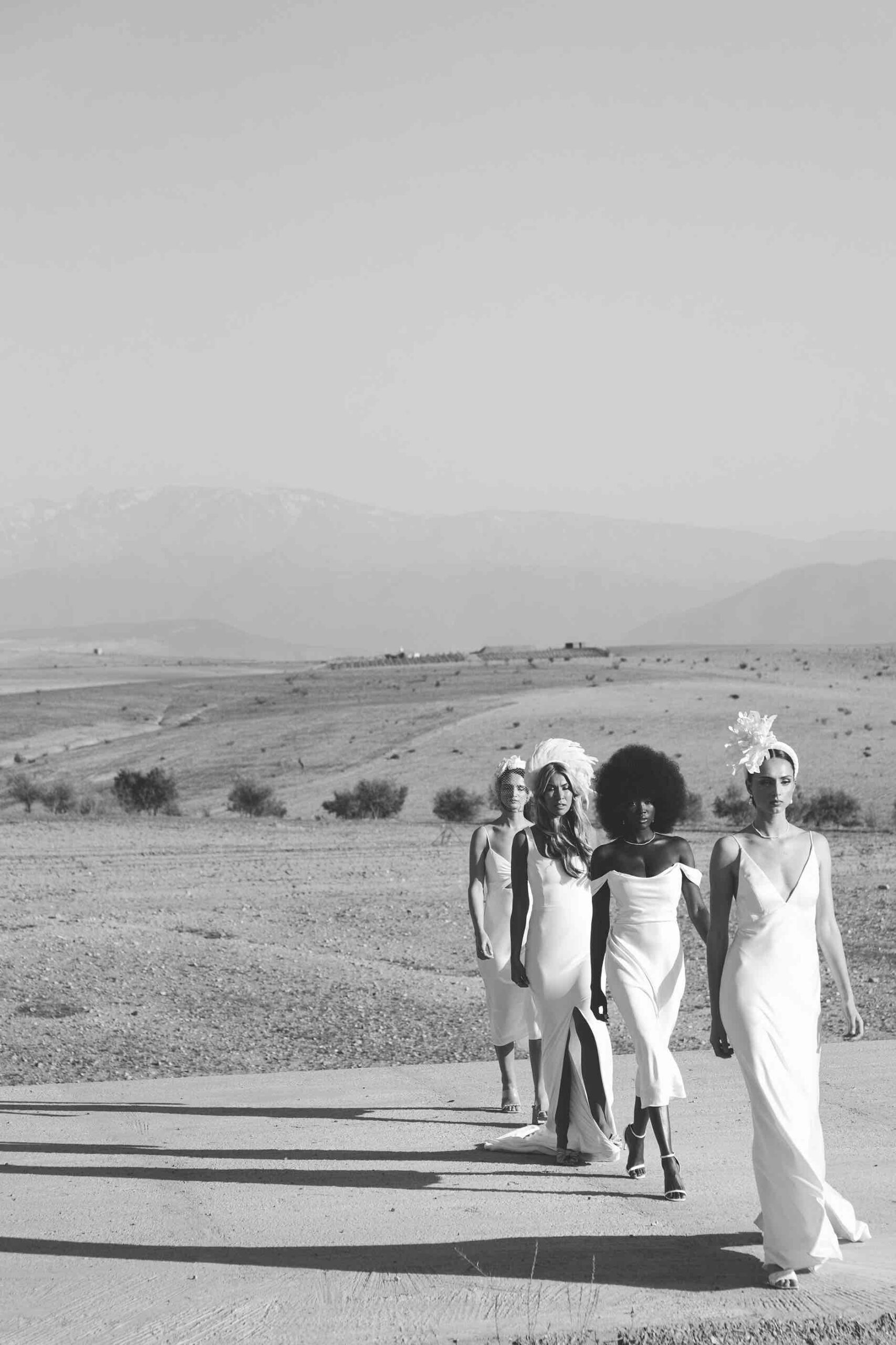 quatre mariées marchent les unes derrières les autres, comme sur un podium de mode, en plein désert - mes prestations de photographe de mariage couvrent même vos envie les plus folles !